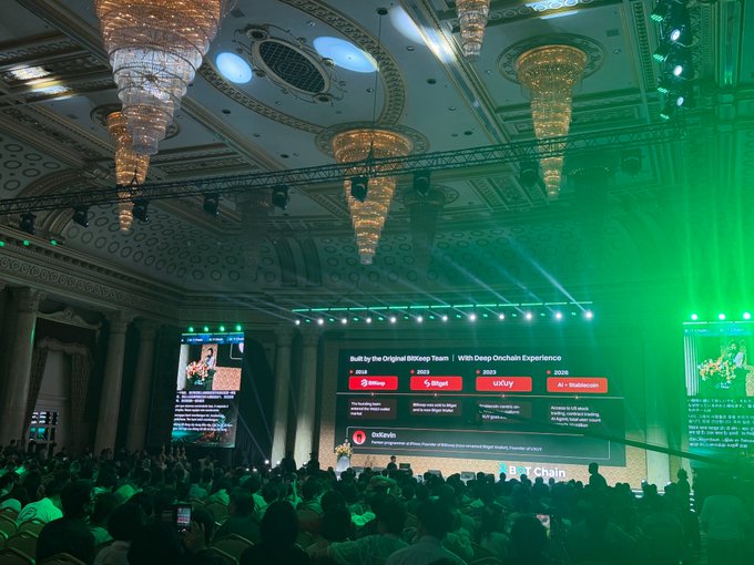 Attendees gather at an elegant, chandelier-lit venue for the Bangkok Summit hosted by @BOTChain_ai, where a large screen displays "Built by the Original BitKeep Team" and showcases partners including Binance, Bitget, CoExy, and GoPlus, with UXUY Co-Founder Vivian presenting on stage about AI and stablecoins in the future of finance.
