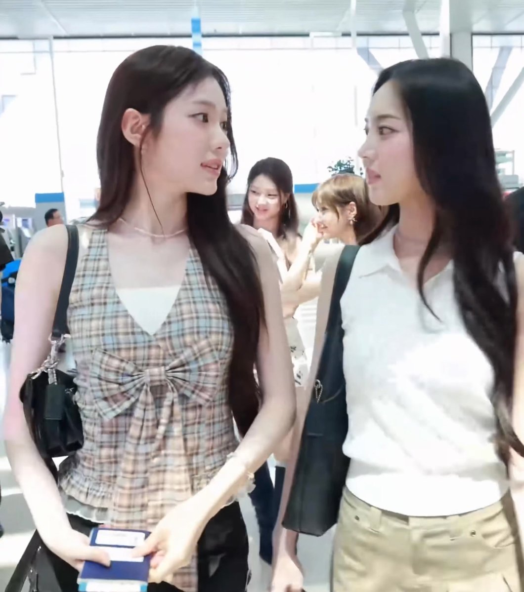 The image shows two young women at what appears to be an airport, with one wearing a plaid top and holding what looks like a passport, while the other wears a white sleeveless shirt. Based on the accompanying hashtags (#이솔 #LEESOL #수이 #SUI #키키 #KiiiKiii), these appear to be members of the K-pop group KiiiKiii, likely traveling for overseas activities.