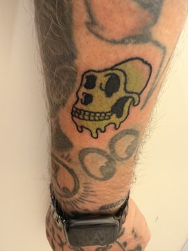 A close-up of a tattoo on an arm featuring a stylized skull, swirls, and other designs, with the person wearing a black smartwatch.