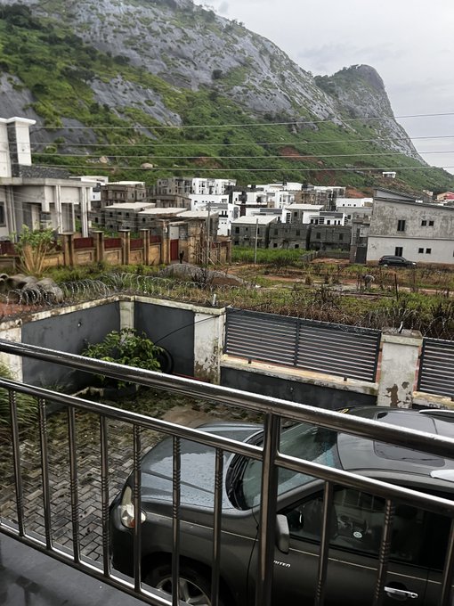 A view from a balcony overlooking a parked car, with a housing development and a rocky hill in the background.