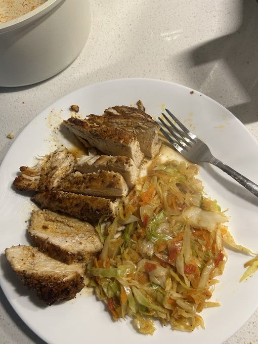 A white plate contains sliced grilled pork tenderloin served alongside a cabbage and carrot slaw, with a fork resting on the side.