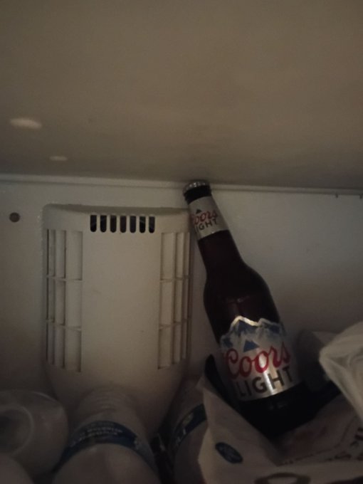 A Coors Light beer bottle sits inside a refrigerator next to other drinks, fitting the "Lock In!" theme of stocking up on beverages.