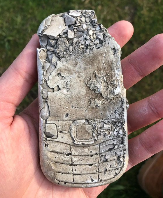 A hand holding a severely damaged Nokia phone, with the top portion broken off, exposing internal components and debris.