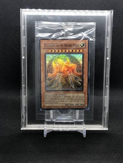 A Yu-Gi-Oh! trading card titled 'Testament of the Arcane Lords' (Spellcaster/Effect) with ATK/3000 DEF/3000 is displayed in a protective acrylic case.