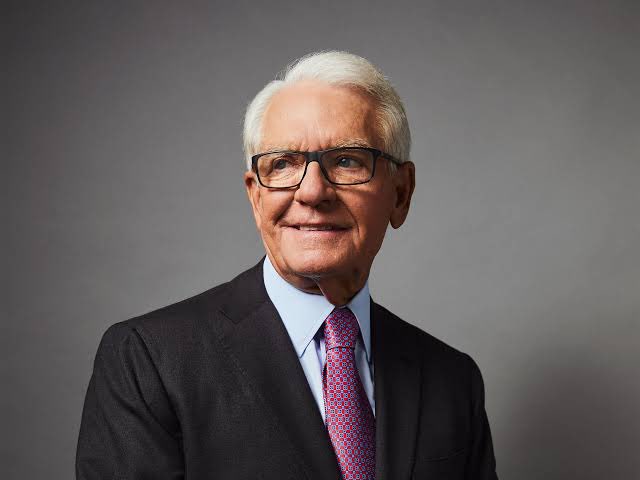 A distinguished older man with white hair, wearing glasses, a dark suit, and a patterned red tie, is pictured in a professional portrait against a gray background. The image likely represents Charles Schwab, the financial figure referenced in the post discussing Senate dynamics around XRP and crypto legislation.