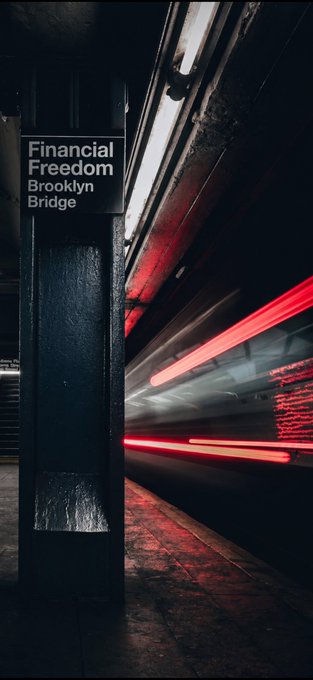 A subway station sign reading 'Financial Freedom Brooklyn Bridge' with motion-blurred red train lights streaking past in the background.