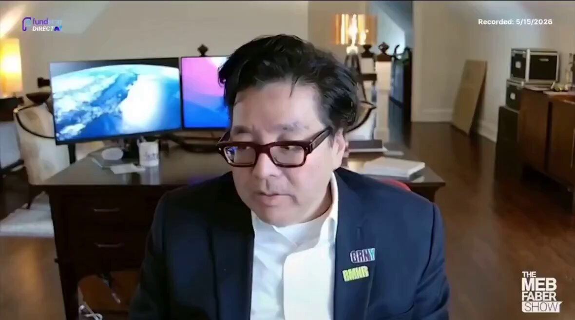 The image shows a man wearing glasses, sitting at a desk with two computer monitors behind him. The man appears to be talking or giving a presentation while looking directly into the camera. There are also some books visible near the man's desk, suggesting that he might be working on a project or studying.