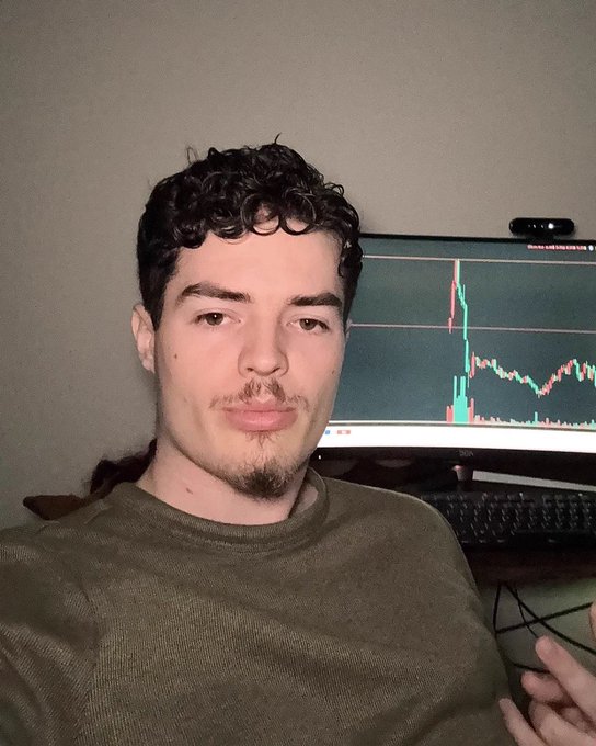 a selfie of a young man in a green shirt sitting in front of a computer displaying a trading chart