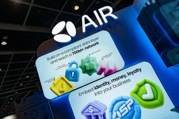 A brightly lit AIR booth display features the company's logo and tagline about being "Built on compact data layer and reach 700M+ network," alongside colorful icons promoting its three core services: Identity, Money, and Loyalty, with the ASE coin branding visible—showcasing the Animoca Brands and Leap collaboration that generated over 500 new AIR accounts during the event.