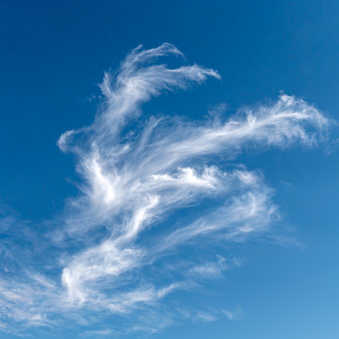 Wispy white cirrus clouds swirl against a clear blue sky.