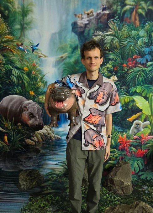 A young man wearing a colorful shirt printed with hippos stands in front of a tropical jungle mural featuring a waterfall, monkeys, birds, and hippos, with a small blue butterfly perched on his shoulder.