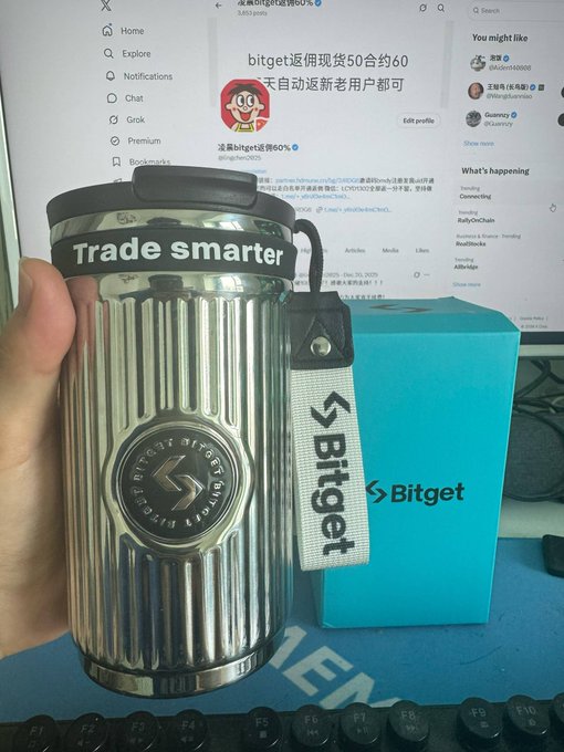 In this image, a person is holding a metal travel cup with the word "Trade" written on it. The cup also has a tag attached that reads "bitget". In the background, there is a computer monitor displaying some information about Bitget's stock trading and other news related to Bitget trading. This suggests that the photo was taken in connection with a post or discussion about Bitget's stock market activities.