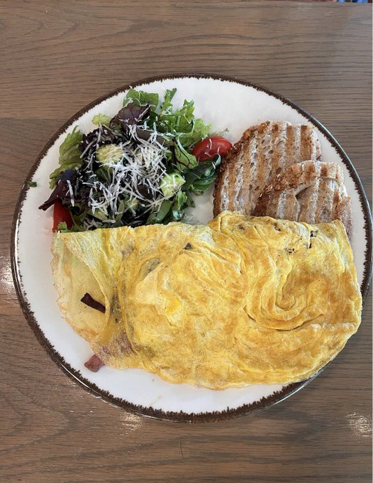 A plated meal featuring a yellow omelet, grilled bread, and a fresh green salad with tomatoes served on a white dish.