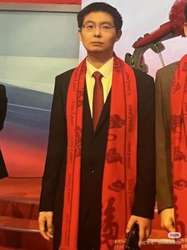 A man wearing glasses, a dark suit, and a red ceremonial scarf stands on stage, likely at an official event or award ceremony, with Chinese characters visible on the backdrop. The image appears to depict Wang Xingxing, the founder of Unitree Robotics, aligning with the post's reference to the founder of the world's top-ranked robotics company.