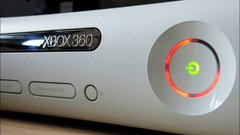 A close-up photo of a white Xbox 360 console showing the power button glowing green with a red ring.
