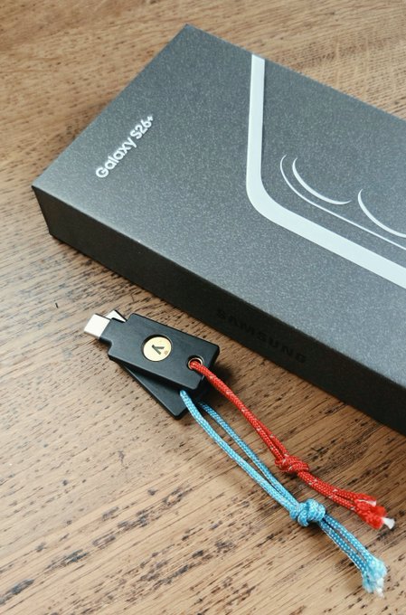 A Samsung Galaxy S24 smartphone box next to two USB-C adapters with red and blue paracord lanyards on a wooden surface.