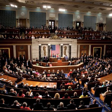 The image shows the interior of the US House of Representatives, likely during a significant address, as members gather on the chamber floor and in the gallery. This setting directly relates to the accompanying post about the House passing legislation 417-3 to require large AI data centers to cover the additional electricity costs they generate, highlighting the chamber where such consequential votes occur.