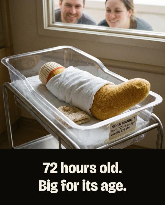 A newborn baby wrapped in a hospital blanket and wearing oversized socks lies in a clear bassinet while two smiling parents peek through the nursery window, with a label on the bassinet humorously marked "SOCK MARKET born 72 hours ago, weight $28.0M." The image playfully personifies a newborn to reflect the cryptocurrency's impressive launch metrics, emphasizing its youth alongside its surprisingly strong $28M debut.