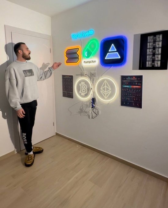 A man gestures toward a wall display of illuminated neon signs featuring "OziLive," "Pump.fun," a blue triangle logo, Bitcoin (₿), and Ethereum (Ξ) symbols, visually tying into the caption's prediction that memecoins are poised for a massive rally.