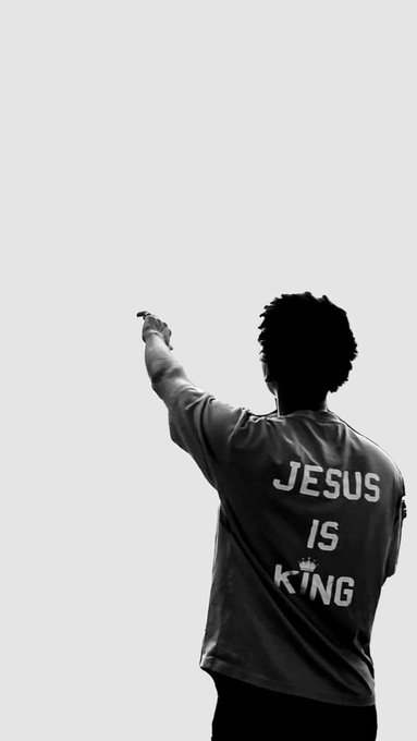 A black-and-white photo of a person from behind wearing a t-shirt that says 'JESUS IS KING' with a small crown symbol, pointing toward a blank white background.