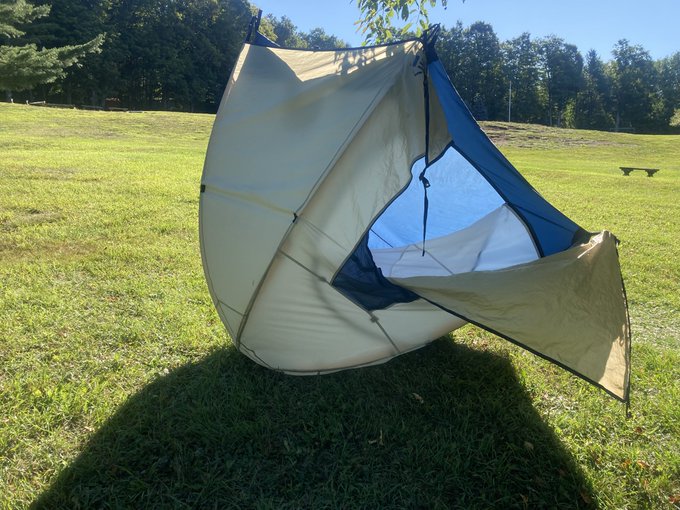 An inverted, dome-shaped camping tent with a partially open door sits upside-down on a grassy field.