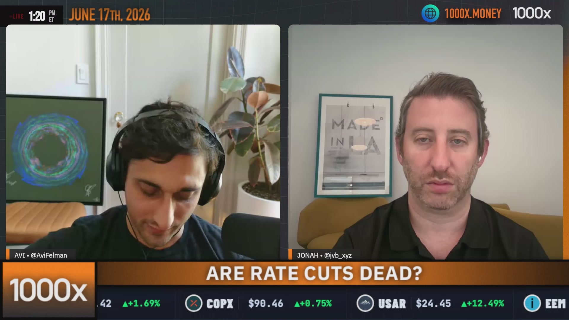 The image shows two men sitting at a desk, both wearing headphones and looking at their computer screens. They appear to be engaged in an online meeting or discussion about current events. The background of the image features a clock with the time displayed as 1:00 pm. There is also a potted plant visible on one side of the room.