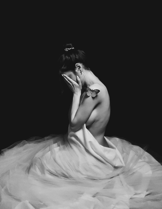 A black and white self-portrait of a woman in a flowing white dress with a butterfly on her shoulder, capturing the essence of the "the things we carry" collection.