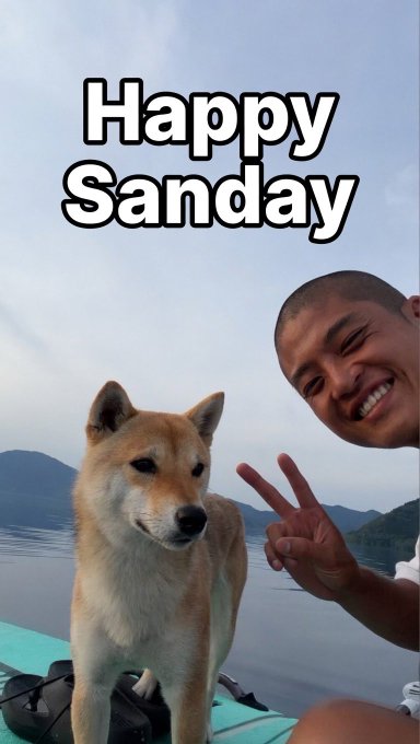 A selfie-style image showing a smiling man making a peace sign next to a Shiba Inu dog, with 'Happy Sanday' text overlaid, taken on a paddleboard on a lake.