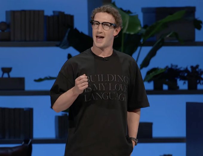 Meta CEO Mark Zuckerberg giving a presentation on stage, wearing glasses and a black t-shirt that reads 'BUILDING IS MY LOVE LANGUAGE'.
