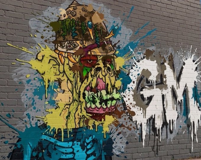 A vibrant graffiti mural on a brick wall features a stylized zombie or monster character with green dripping slime, surrounded by colorful paint splatters.