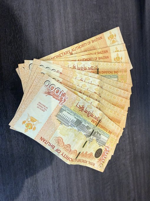 A fan of various Bhutanese ngultrum banknotes spread out on a dark wooden surface.