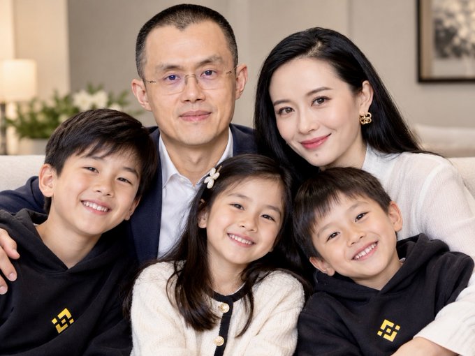 A family portrait showing two parents and three children smiling at the camera in a well-lit room.