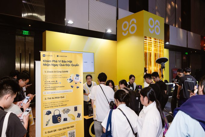 Crowds gather at the Coin98 booth at what appears to be the Conviction Vietnam event, examining a banner advertising a "Check-in" gift promotion with listed steps (1. Check-in Cùng Coin98, 2. Thử Sự Nhẫn Nại, 3. Quẹt QR - Sẵn Giải Đặc Biệt) in Vietnamese, while a neon-lit display in the background prominently showcases the numbers "98" and "96." Staff and attendees interact throughout the booth, capturing the bustling atmosphere the post describes of thousands of conversations and countless check-ins over the two-day event.