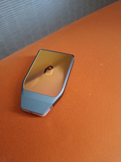 A Ledger hardware wallet (marked with the "L" logo) rests on an orange surface against a blue textured background. The image illustrates the post's reflection on sticking with Ledger out of convenience and familiarity rather than thorough research.