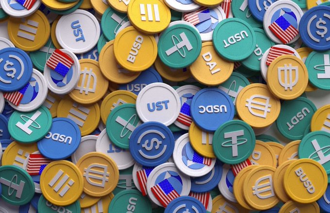 A pile of colorful 3D-rendered stablecoin tokens—including USDC, USDT, USDP, BUSD, and TUSD featuring American flag designs—representing the rapidly expanding stablecoin market that CZ predicts could grow "a couple of thousand times."