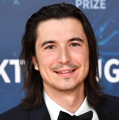 A man with long dark hair and a mustache smiles at the camera while wearing a black tuxedo and bow tie, standing in front of a backdrop partially showing the word "PRIZE." The image appears unrelated to the post, which highlights Robinhood ($HOOD) achieving $2.67 billion in DEX trading volume, as no branding, text, or context about the company is visible.
