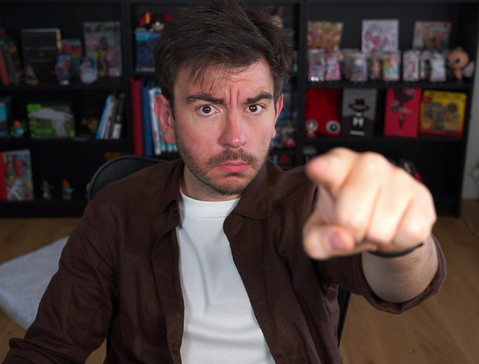 A man with a stern, intense expression points directly at the camera, mimicking the classic "pointing-at-you" meme to command the viewer to buy a coin called "Normies." Behind him, shelves filled with collectibles and figures frame his assertive posture, reinforcing the playful yet firm tone of the post urging the audience to invest.