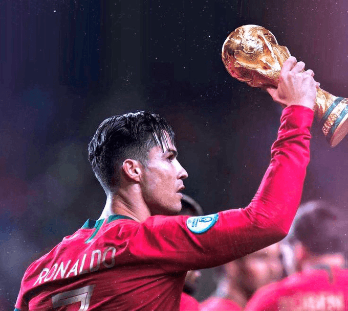 Cristiano Ronaldo wearing a red jersey with "RONALDO" and "7" on the back holds the FIFA World Cup trophy aloft in celebration.