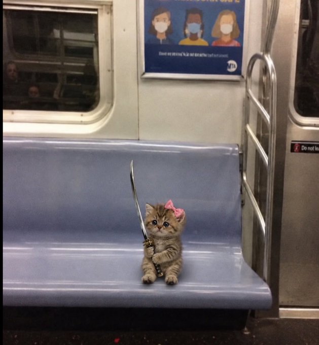 A small tabby kitten wearing a pink bow sits on a blue subway seat while holding a katana sword, with a poster encouraging the use of masks visible above.
