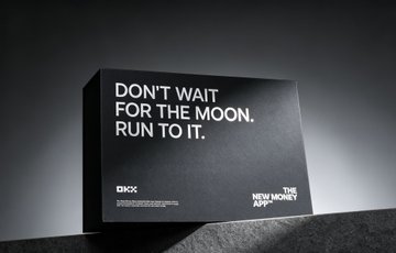 A black DMCC advertisement reading 'DON'T WAIT FOR THE MOON. RUN TO IT.' with 'THE NEW MONEY AG' logo visible.