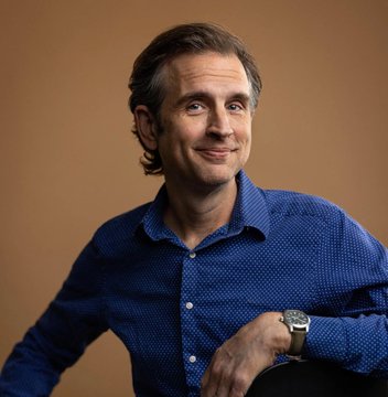 Portrait of Zcash founder Zooko Wilcox in a blue shirt against a warm brown background, visually accompanying the post’s “Reason #107 to choose Zcash: Zooko is a genius