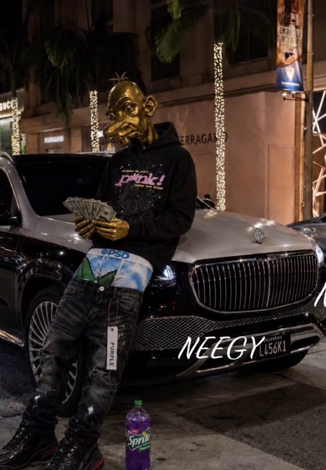 A person wearing a large cartoon mask, a black 'PUNK!' hoodie, and distressed jeans holding cash while leaning against a black Mercedes-Maybach SUV at night, with a Sprite bottle on the ground.
