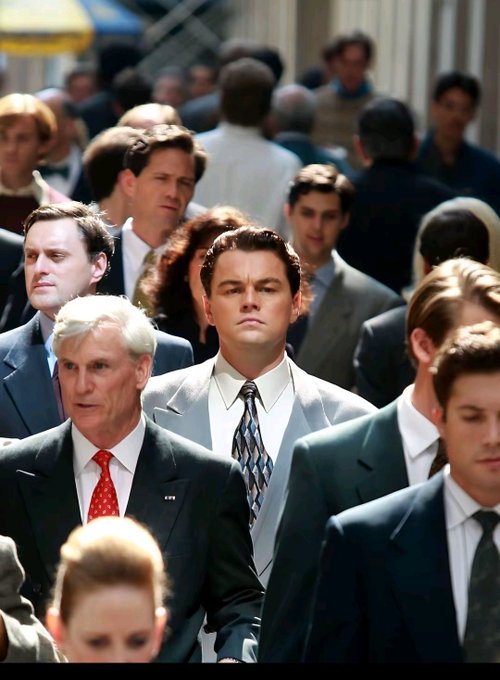 A still from the movie The Wolf of Wall Street showing Leonardo DiCaprio walking through a crowd of businesspeople in suits.