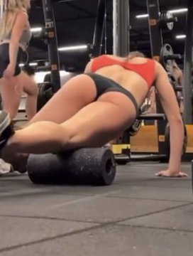 A woman in a red sports bra and black shorts uses a foam roller on her thigh at a gym, while another person walks in the background. The image is used to illustrate the post's complaint about women wearing revealing clothing in public spaces like gyms.