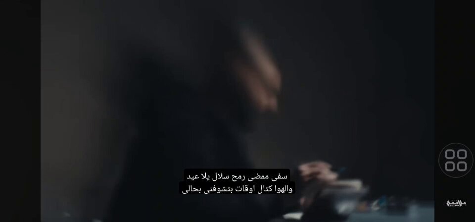 The image shows a man sitting at a table with his hands near a cup, possibly holding a pen or writing something down. The background of the image appears to be dark, which contrasts with the man's presence. There are also some words written in Arabic on the image that seem to be related to the post.