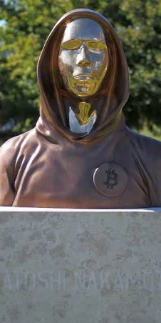 A bronze statue of a hooded figure with a reflective gold face sits on a stone pedestal inscribed with 'KENJI NAKAMURA'.