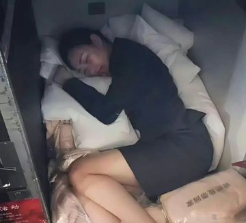 A flight attendant in uniform sleeping in a cramped crew rest compartment on an airplane.