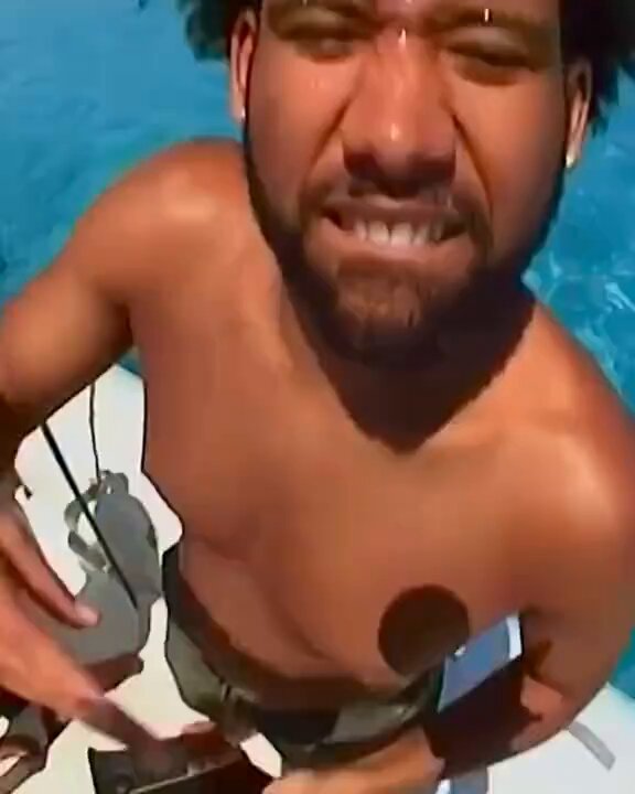 The image features a shirtless man with a beard holding a surfboard while standing in front of a body of water. The man appears to be wearing shorts as well. He has a cell phone attached to his ankle, which might have been used for capturing this moment or communicating with someone else. The post seems to be about the man's surfing experience and possibly related to cryptocurrency trading.