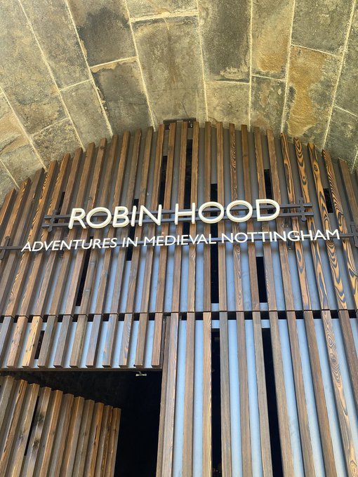 A photograph of a wooden slatted architectural structure with an illuminated sign reading 'ROBIN HOOD - ADVENTURES IN MEDIEVAL NOTTINGHAM' mounted on it.