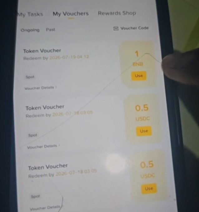 A smartphone displays Binance's "My Vouchers" page showing three Token Vouchers—a 1 BNB voucher and two 0.5 USDC vouchers—ready to be redeemed, aligning with the caption celebrating receiving 1 BNB ($572) from Binance's rewards program.